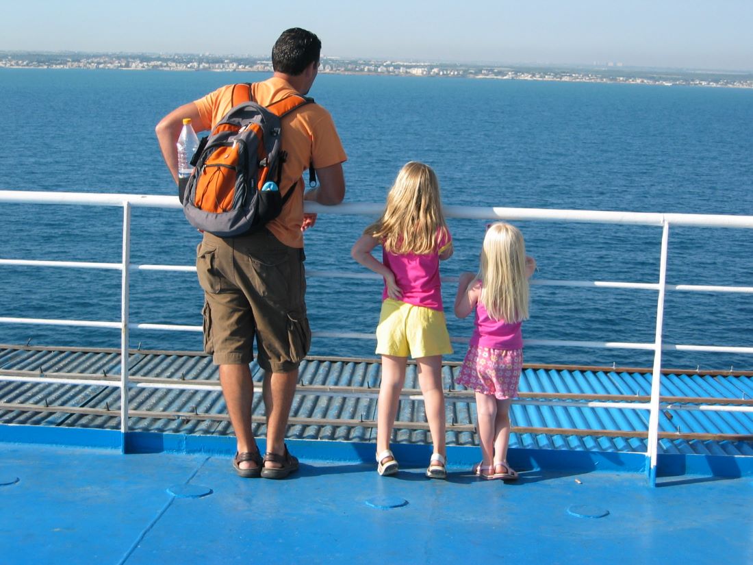 A dad  and two young daughters all looking at the coastline on the horizon from a boat deck | Tips for traveling full-time with kids from Kaitlin Murray for Wanderful
