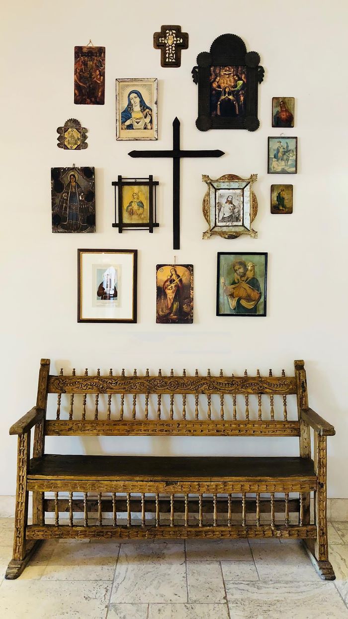 A retablo in New Mexico: A small bench below a variety of framed religious images and a wooden cross all hanging on the wall