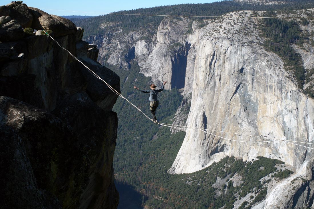 A tight rope walker is mid-way across a line strung in Yosemite National Park at Taft Point.
