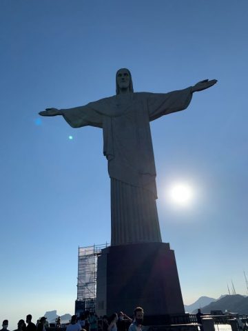 Christ the Redeemer statue in Rio de Janeiro, with Milagros Rojas sitting at the top step below it.