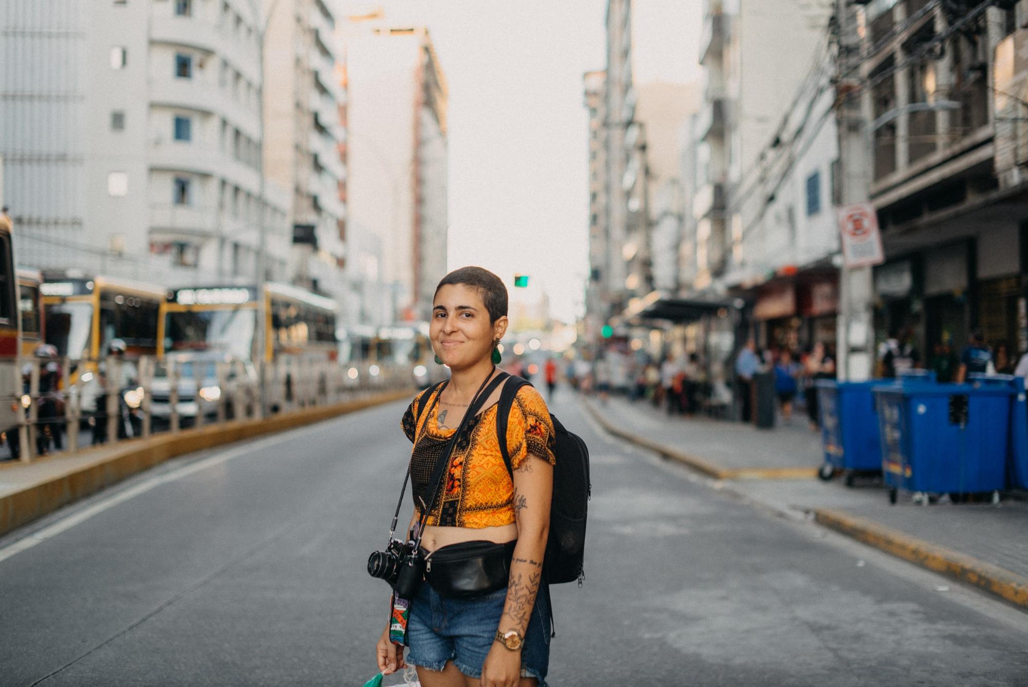 Photographer Céu Albuquerque standing in the middle of a city street with camera gear draped around her