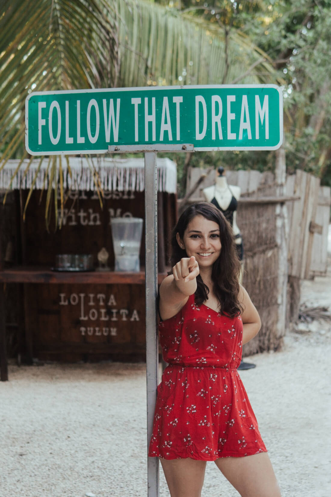 Stacey Valle pointing at the camera while standing under a sign that says Follow that dream