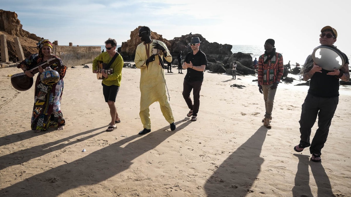 Group of people with long shadows playing music standing in the sand. Surabhi Ensemble in Senegal - photo by Larissa Rolley, photography course creator at Wanderful