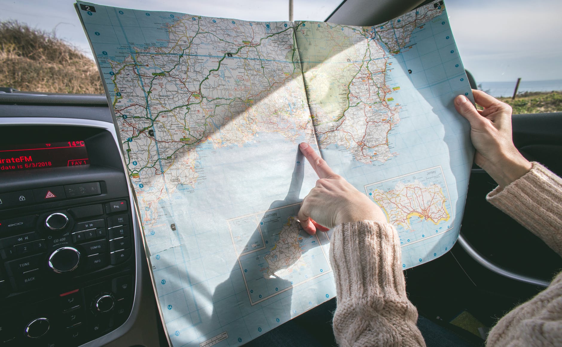 person wearing beige sweater holding map inside vehicle - solo road trips tips from travel experts via Wanderful