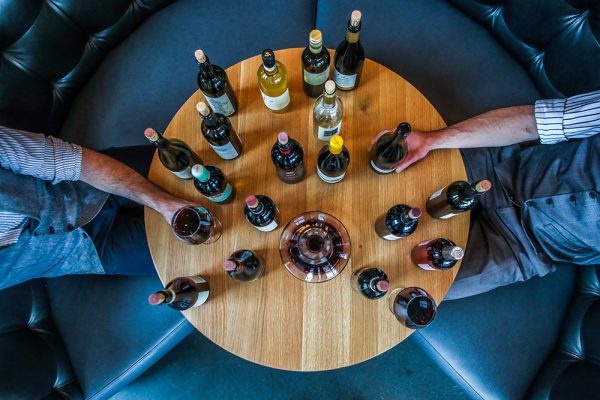 Table full of wine bottles with men's hands reaching out