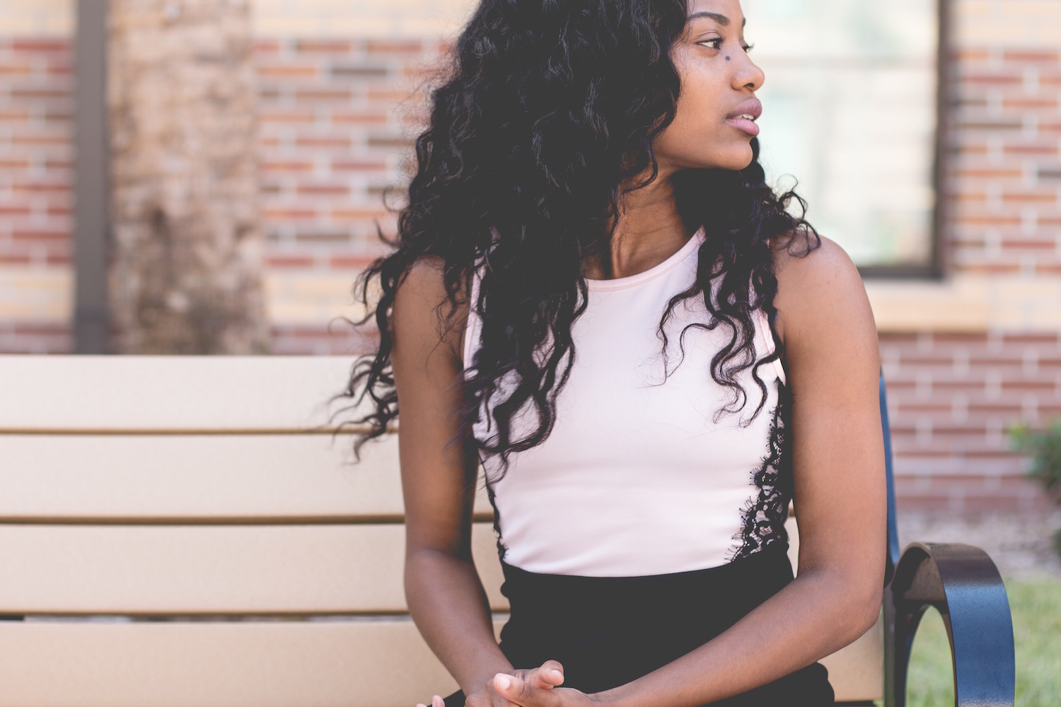 Black women who travel - a close-up of a Black woman with long curly hair sitting on a bench