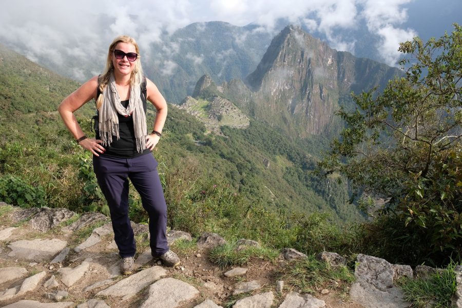 Paulette Perhach poses in front of a lush mountain vista with Macchu Picchu below