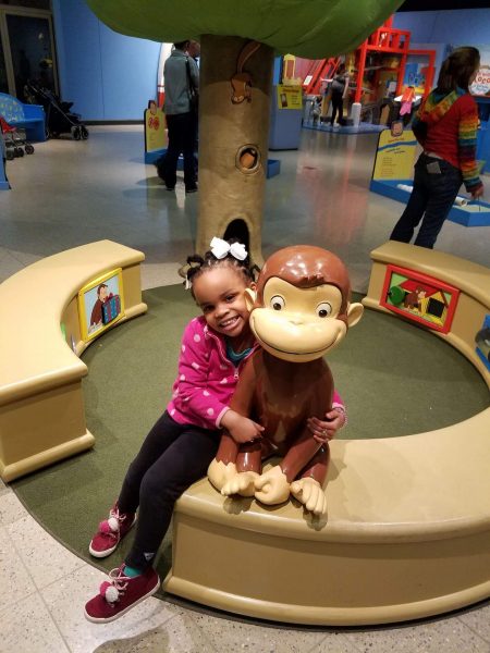 The author's daughter posing with Curious George at the Discovery Center Museum